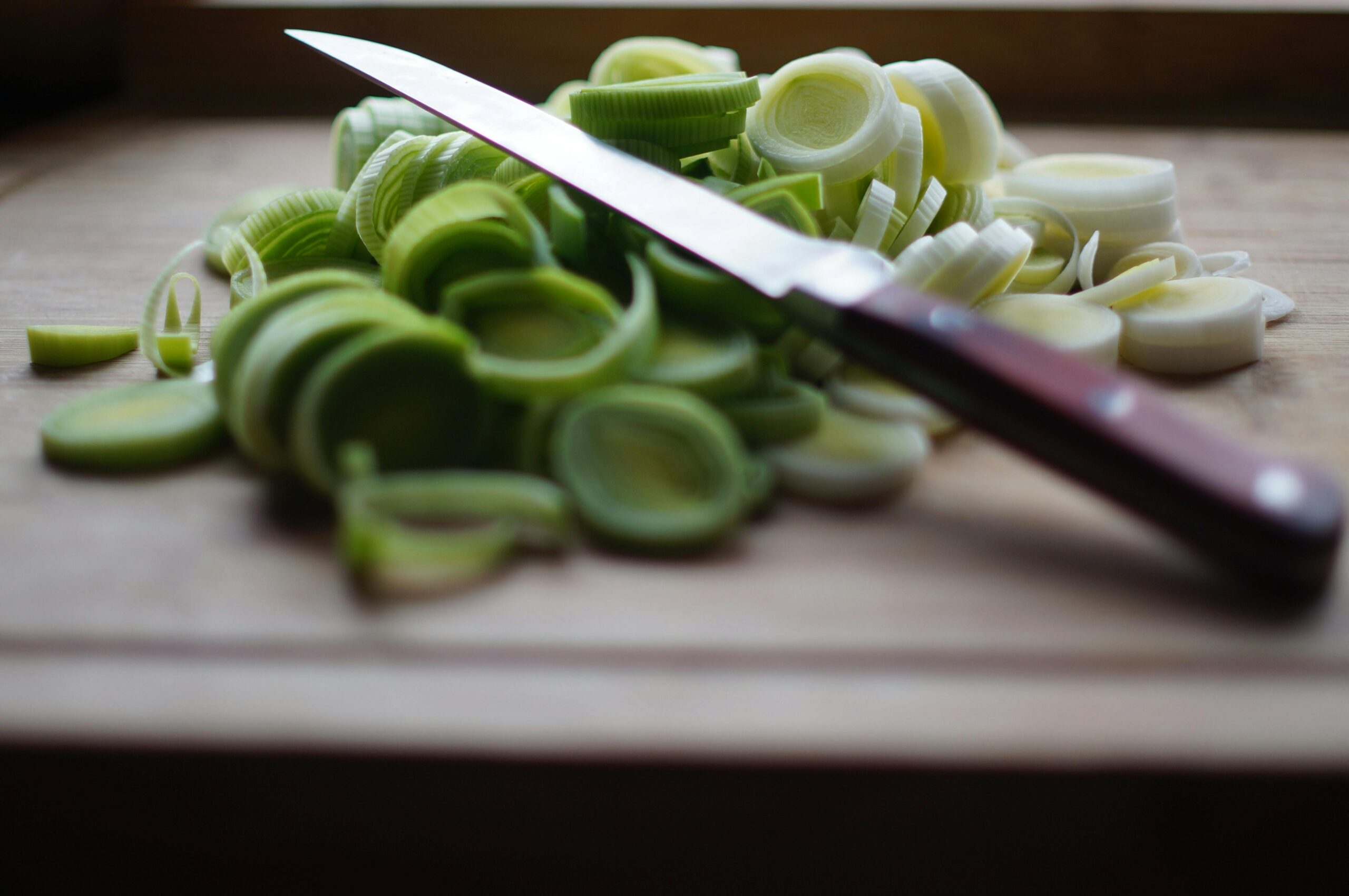 Freshly sliced leeks on a wooden cutting board with a sharp knife, ideal for cooking and food preparation themes.