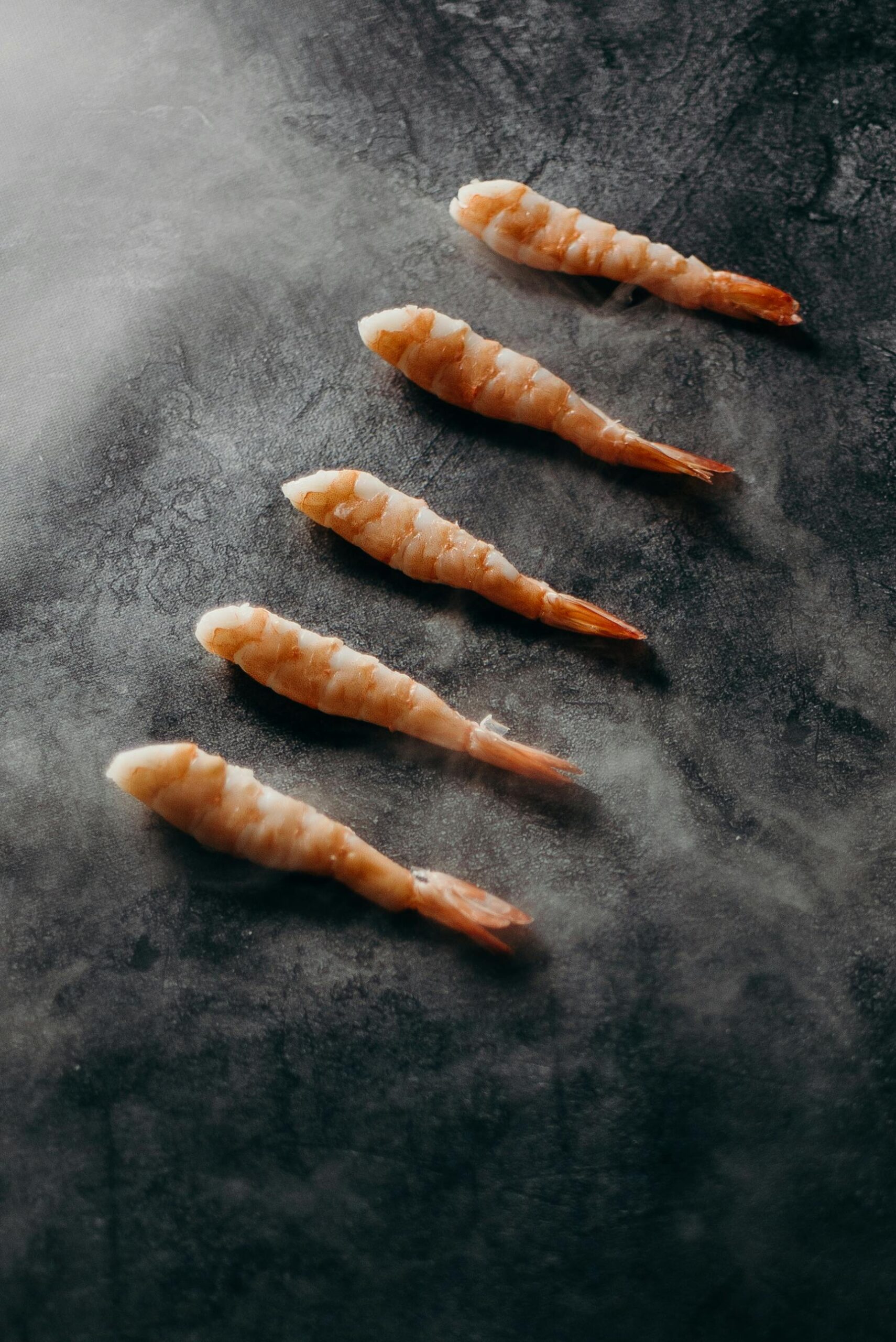 Freshly cooked prawns arranged elegantly on a dark slate surface, captured in a gourmet food style.