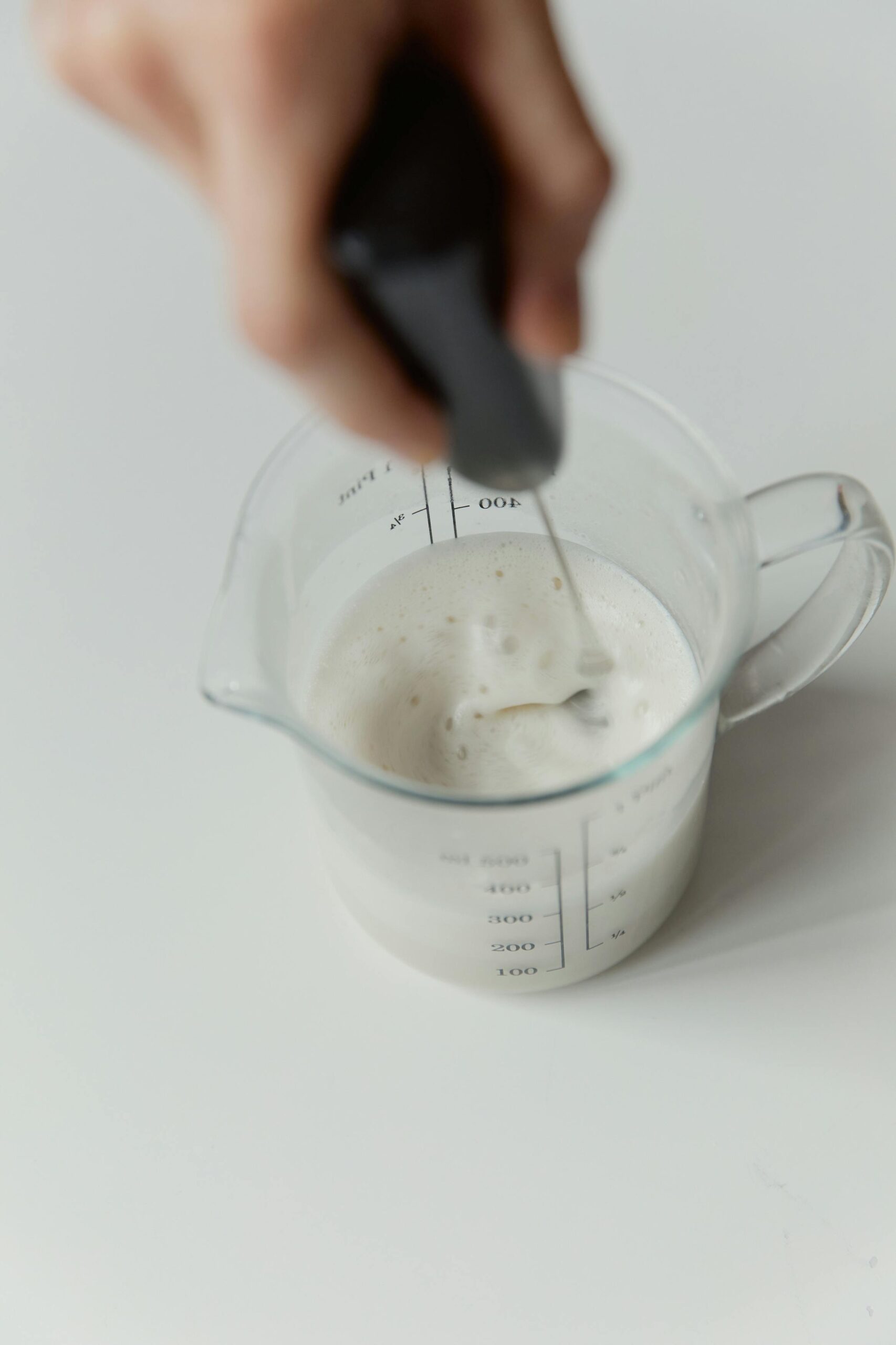 Close-up of a hand frothing milk in a measuring cup, high angle view.